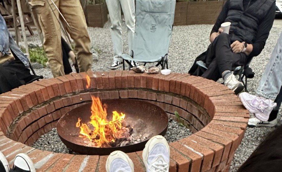 Open campfire burning inside a circular brick fire pit, with visitors cropped above the shoulders