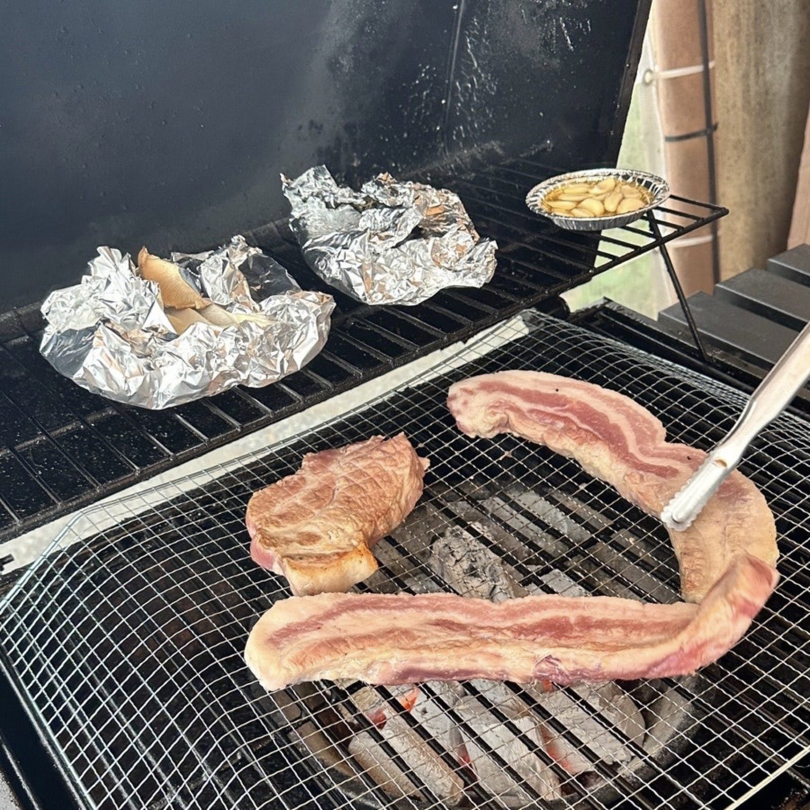 Pork and foil-wrapped food cooking on a charcoal grill