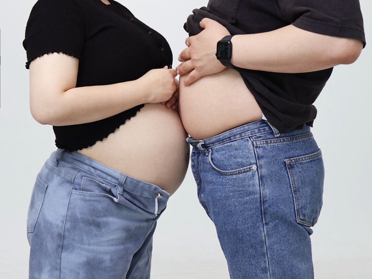 Cropped black-outfit maternity photograph showing two parents from the shoulders down