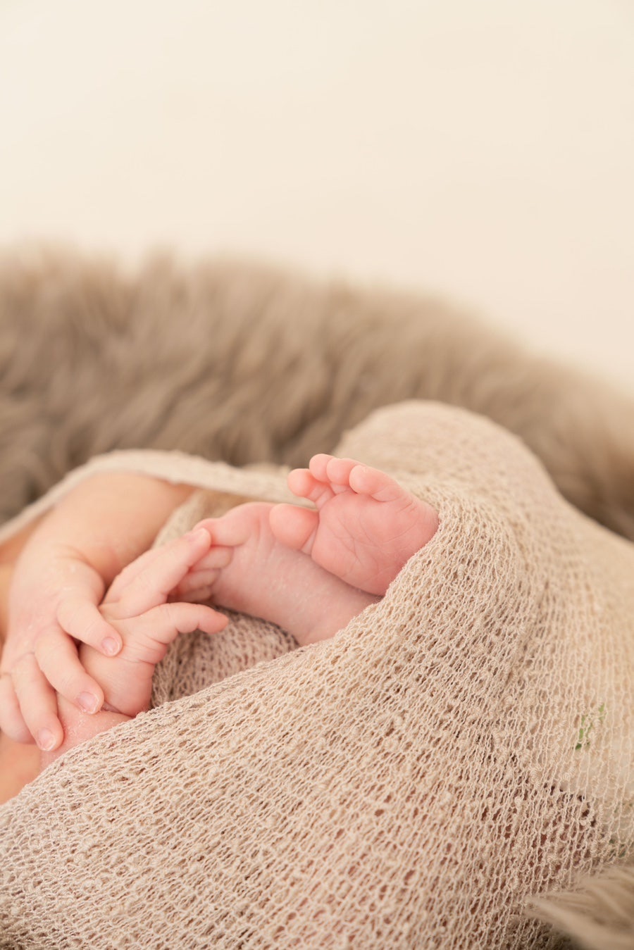 Close detail of a newborn's hands and feet wrapped in a beige knit blanket