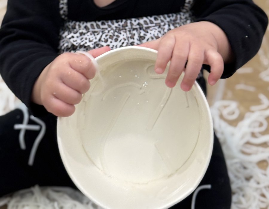A baby's hands holding a bowl after a noodle sensory-play activity