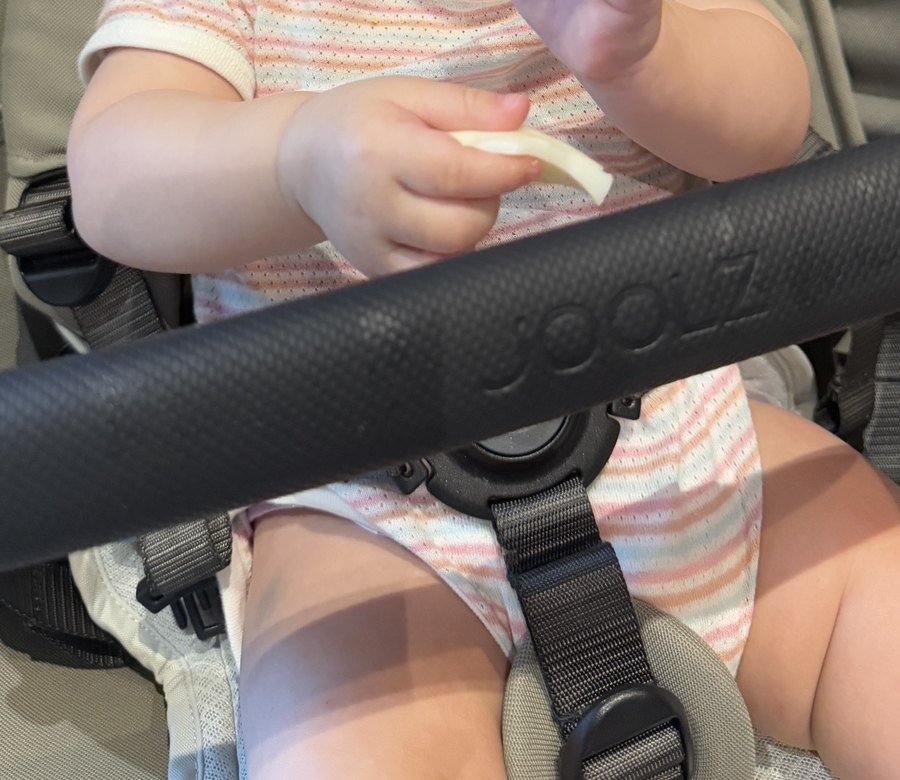 A baby's hands holding a piece of boiled egg in a stroller at breakfast