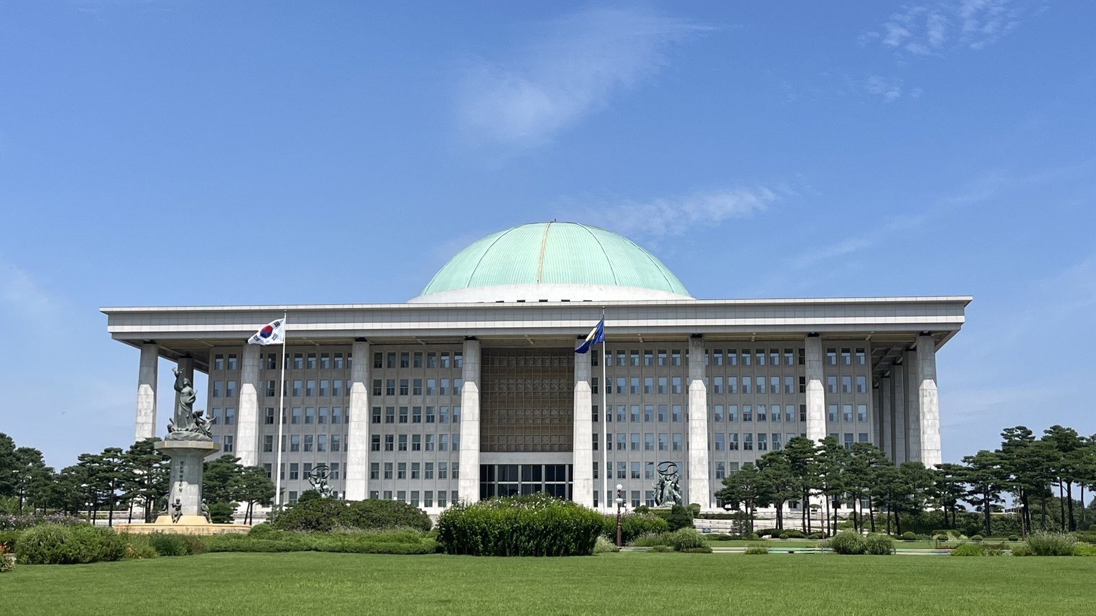 The domed National Assembly Building in Yeouido, Seoul, seen across its lawn under a clear blue sky