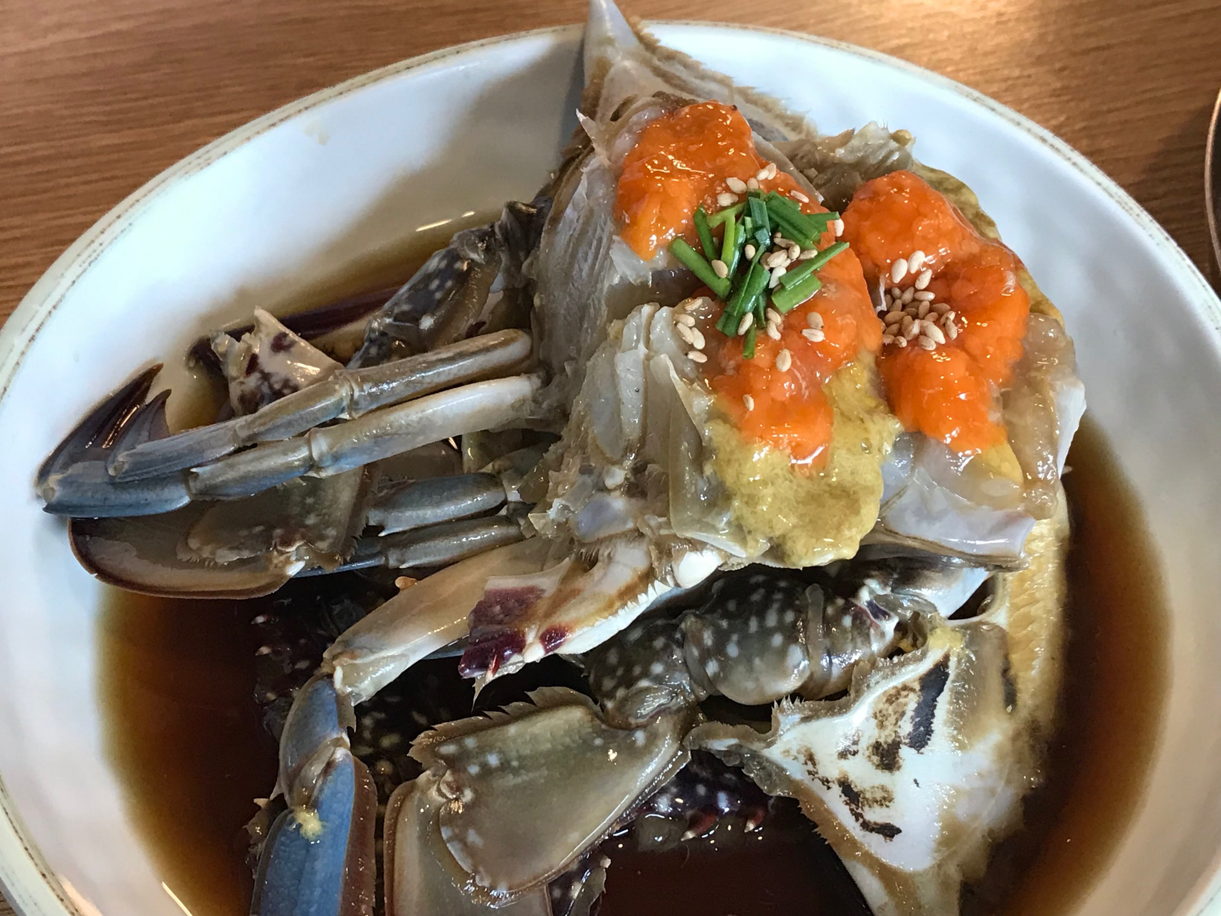 Ganjang-gejang: halved raw crabs glossy with soy marinade arranged in a dark bowl, roe visible in the shells