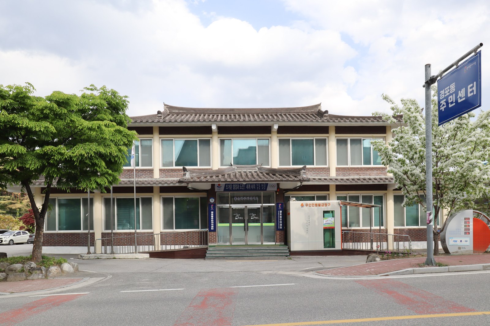 A neighbourhood community service centre with a street sign and an unmanned civil-document kiosk beside the entrance