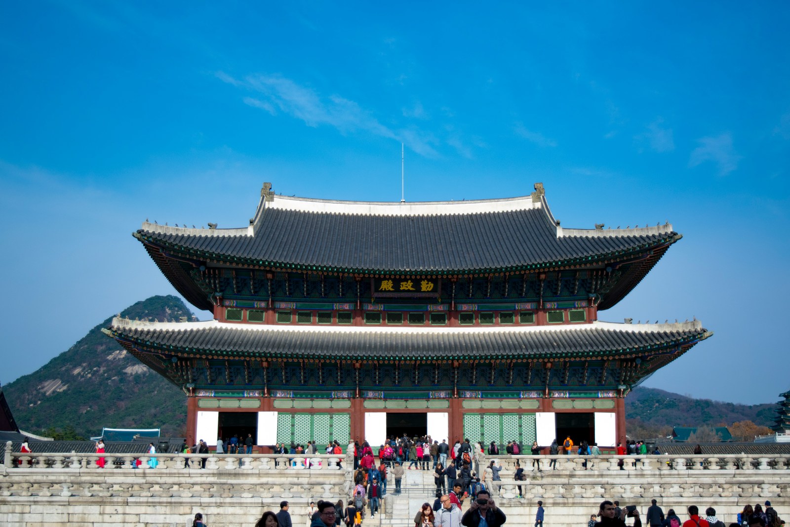 Geunjeongjeon, the two-tier throne hall of Gyeongbokgung palace, on its stone terrace under a clear sky with visitors below