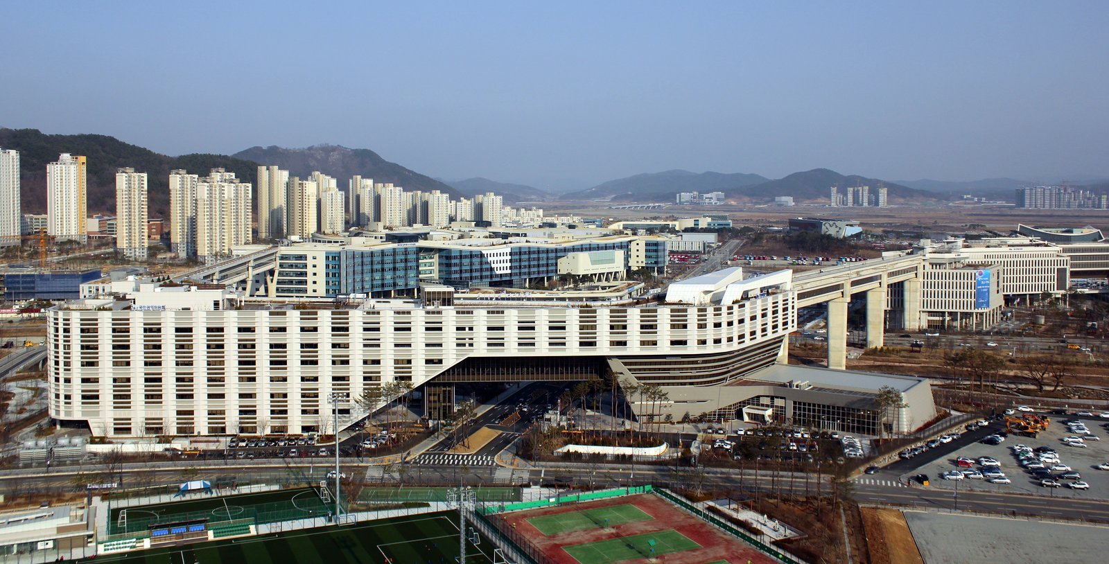 Wide daytime view of the Government Complex Sejong with apartment blocks and hills behind it