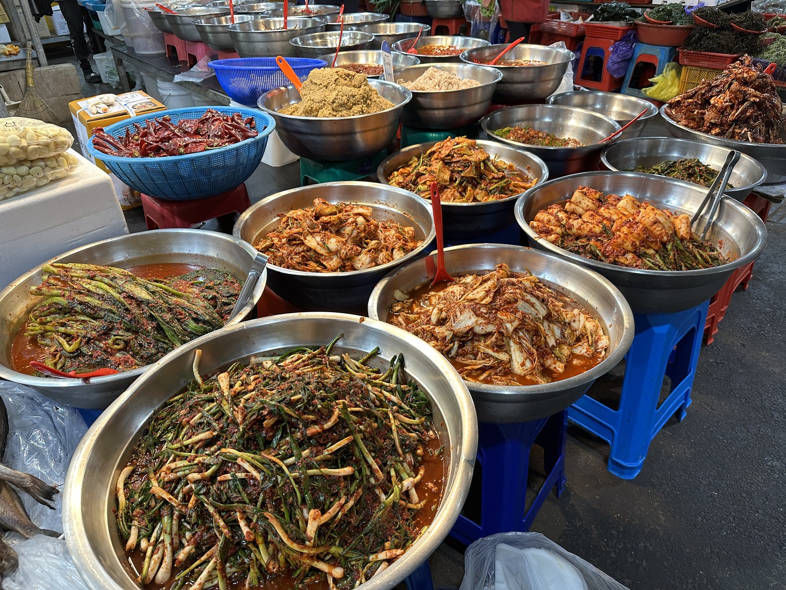 Rows of stainless bowls piled with kimchi, seasoned vegetables and pastes at a banchan stall in Seogwipo Rural Five-Day Market