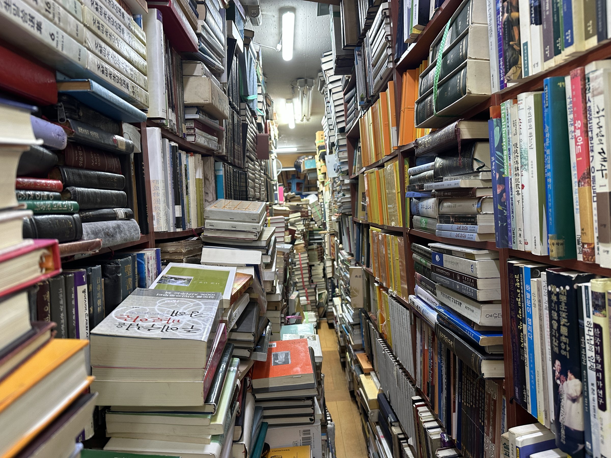 Densely packed shelves of secondhand books lining both sides of a narrow Seoul bookstore aisle