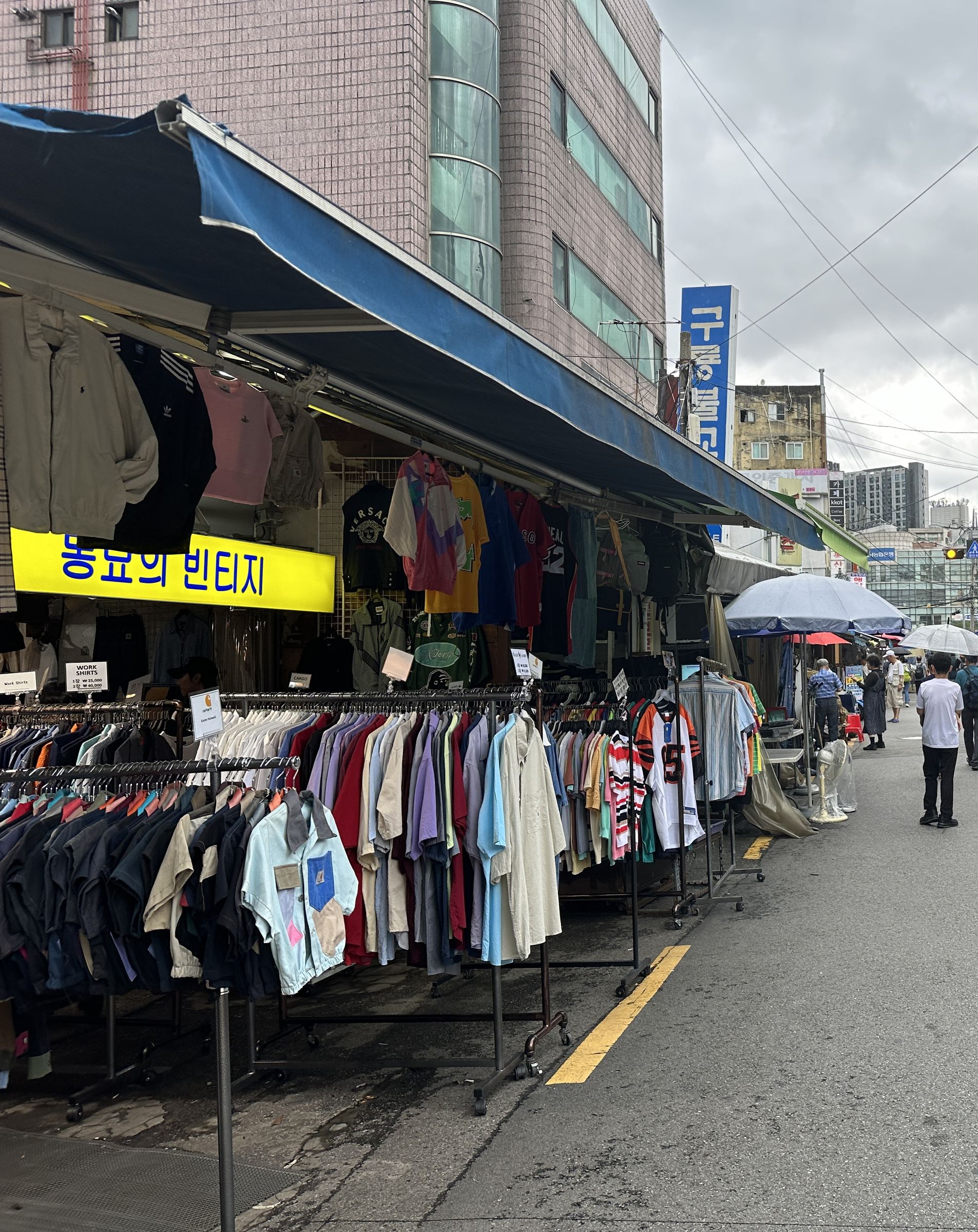 Street-side racks of secondhand vintage shirts and jackets under a shop awning at a Seoul market
