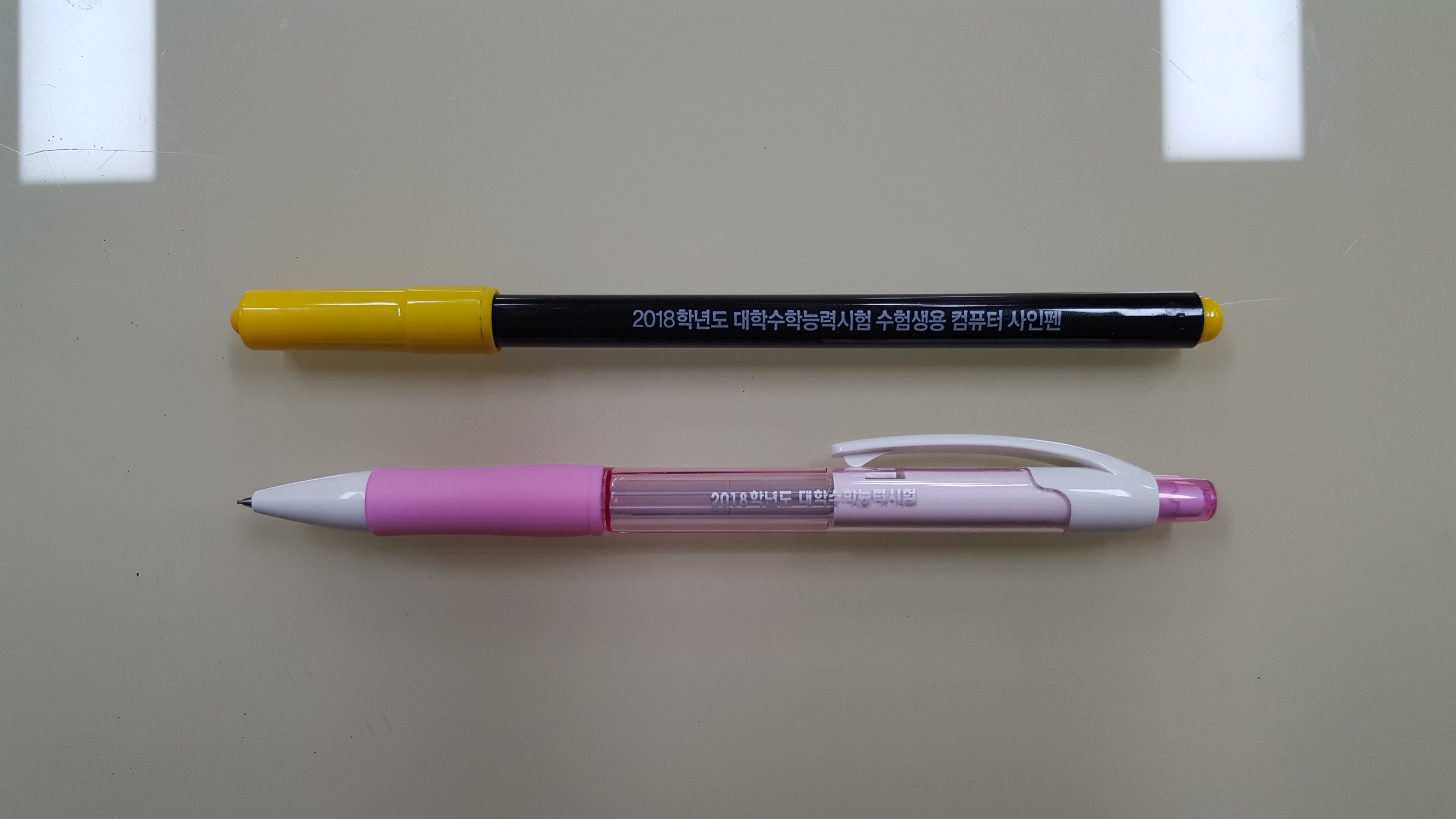 The official exam-issued black computer marking pen and a pink mechanical pencil lying together on a wooden desk