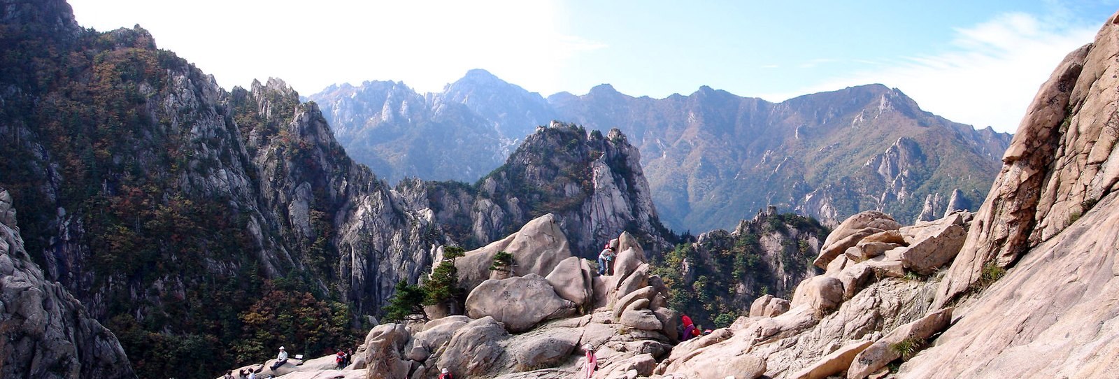 Wide view of granite peaks and ridgelines in Seoraksan National Park seen from a bare rock shoulder, with forested slopes filling the valleys