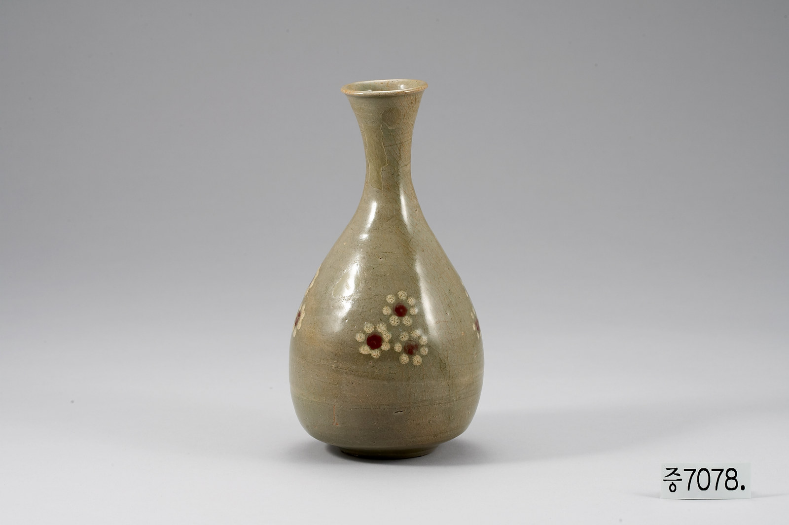 Goryeo celadon bottle with a slender neck and flared mouth, its olive-green body decorated with small flowers made of dark red centre dots ringed by pale dots, beside a museum inventory card reading 증7078
