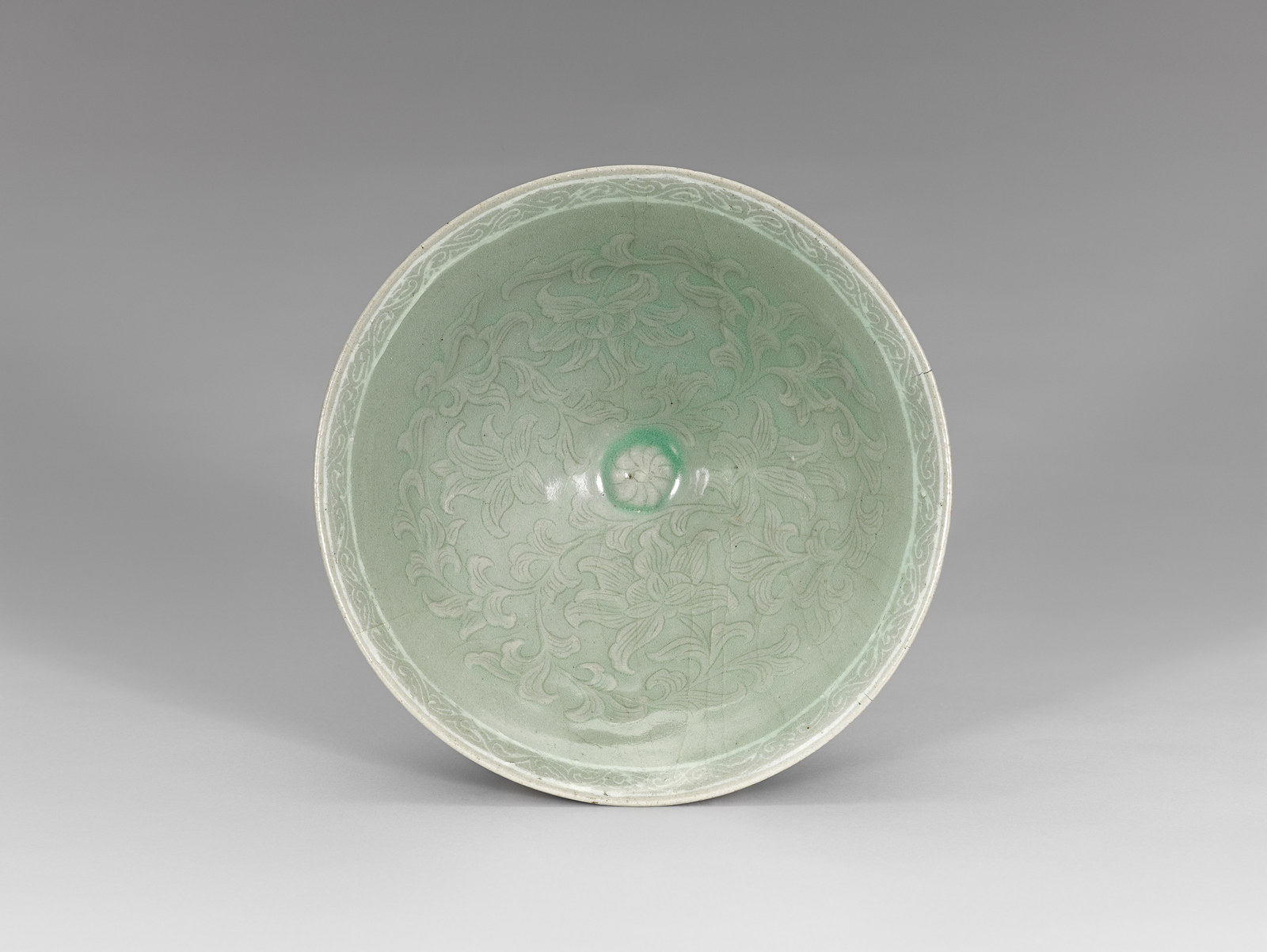 View into a Goryeo celadon bowl from above, its pale green inside covered with a dense scroll of flowers and leaves around a small central rosette, with a pale band and narrow scroll border inside the rim